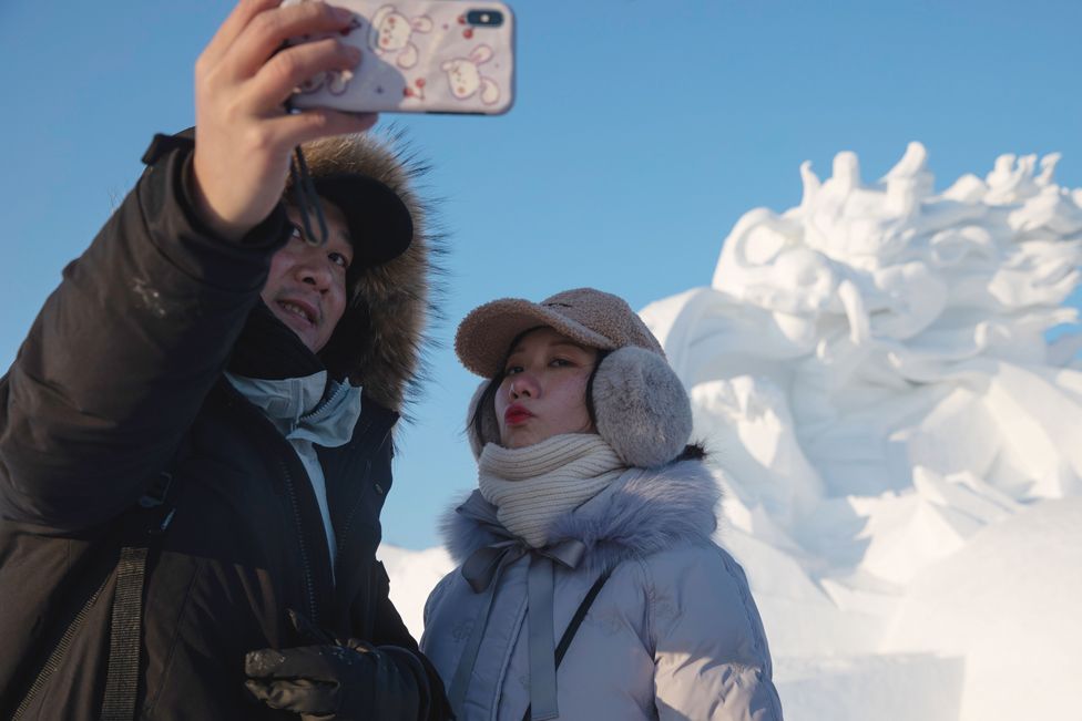 Two people take selfie in front of a snow sculpture