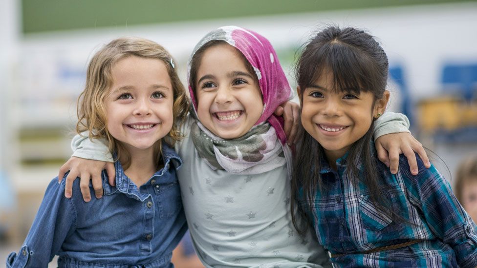 Girls smiling - one white, one in a hijab, one Asian
