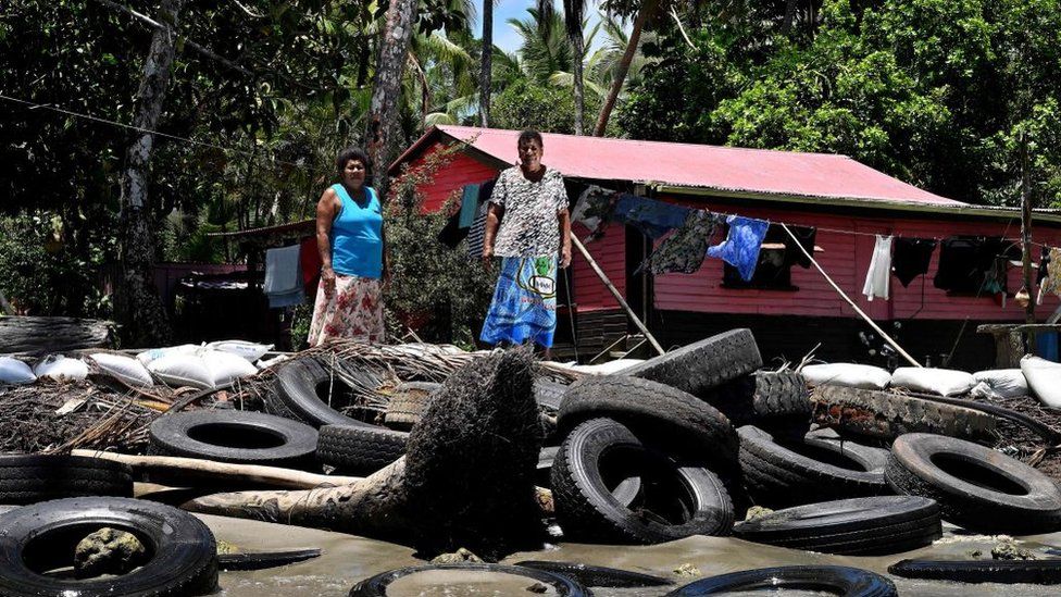 Resident Lavenia McGoon (R) with a family member standing past a makeshift seawall of old rubber car tyres to prevent erosion, outside her beachfront house at a village in the coastal town of Togoru, some 35 kilometres from Fijis capital city Suva.