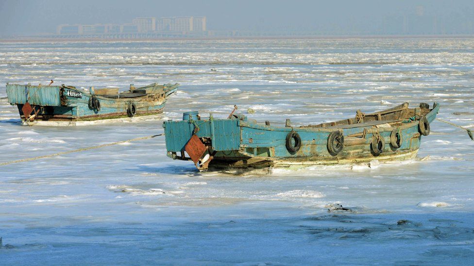 Fishing boats sit stuck in the ice of the frozen coastal waters of Jiaozhou Bay in Qingdao in eastern China's Shandong province on 25 January 2016