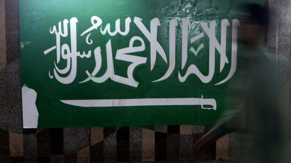 A man walks beside the Saudi flag in Jeddah, Saudi Arabia, 9 December 2015