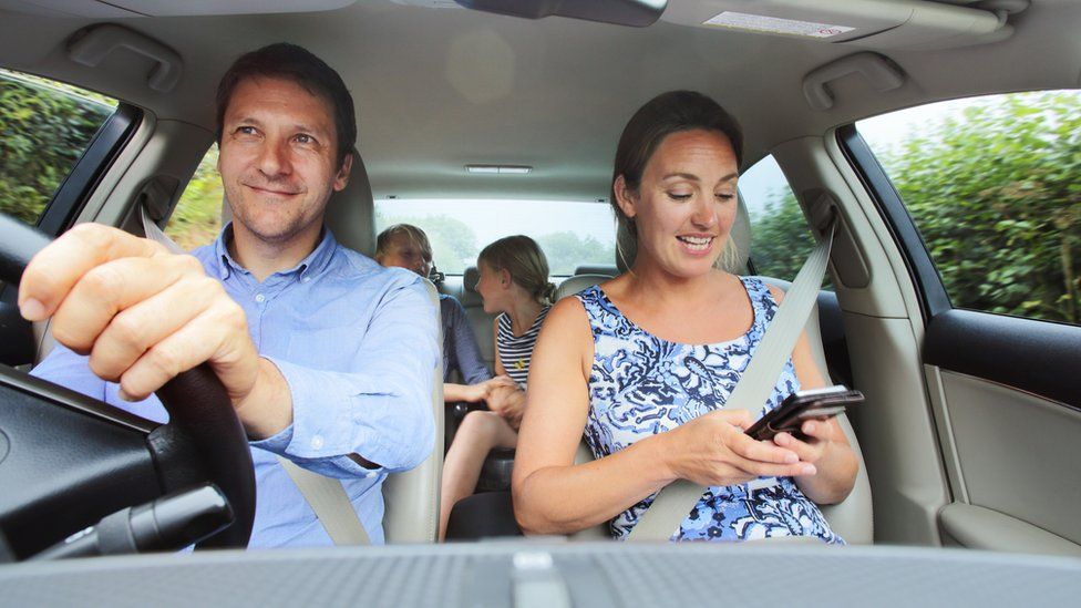 Family in car, mum looking at phone - stock photo