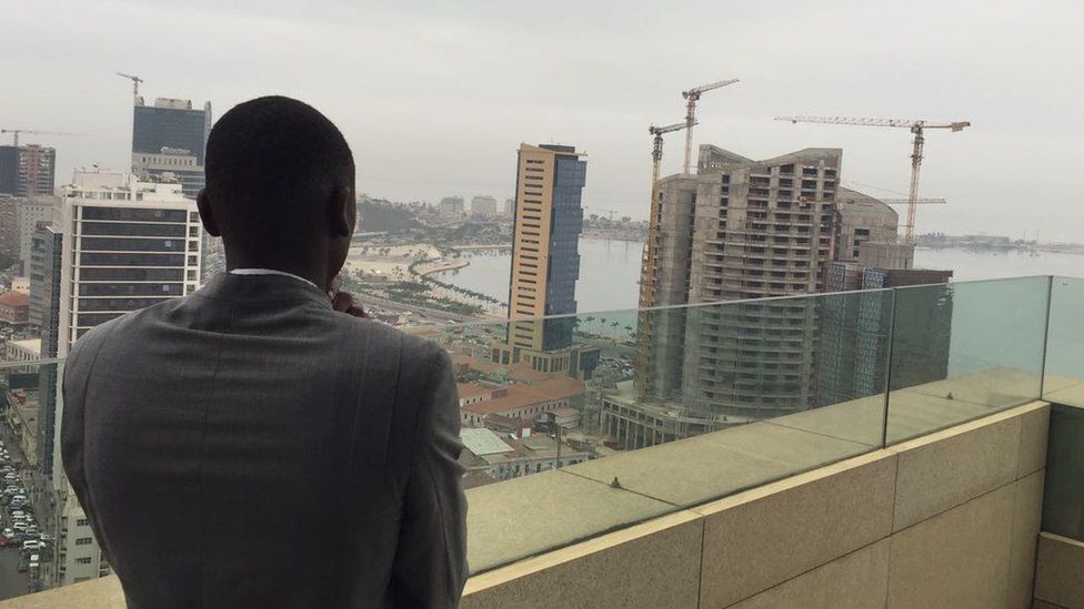 Half-built skyscrapers in Luanda, as a man in a suit looks on
