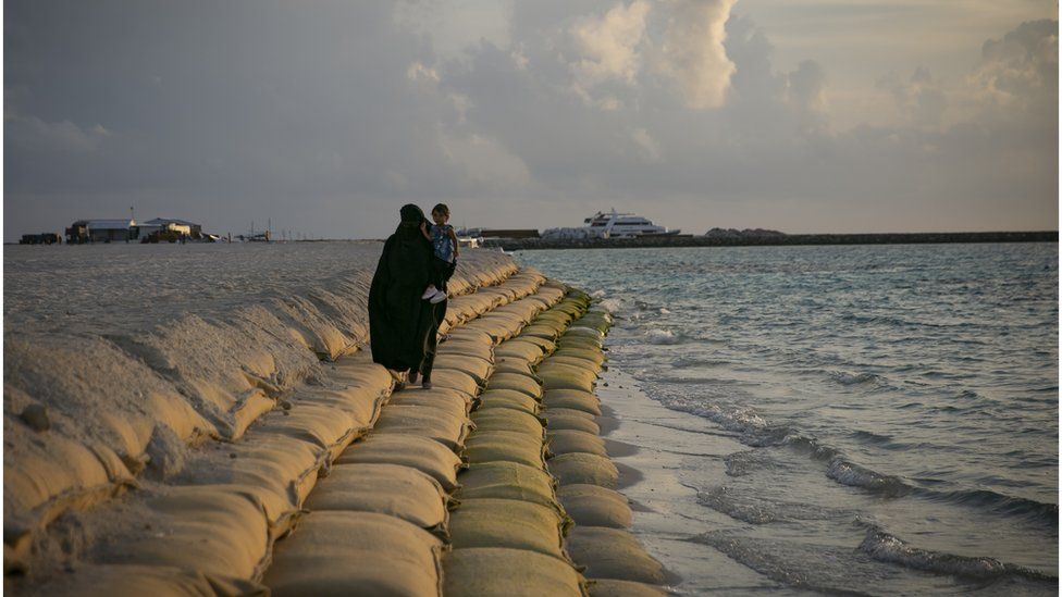 A woman walks on a wall of sandbags, placed to prevent erosion