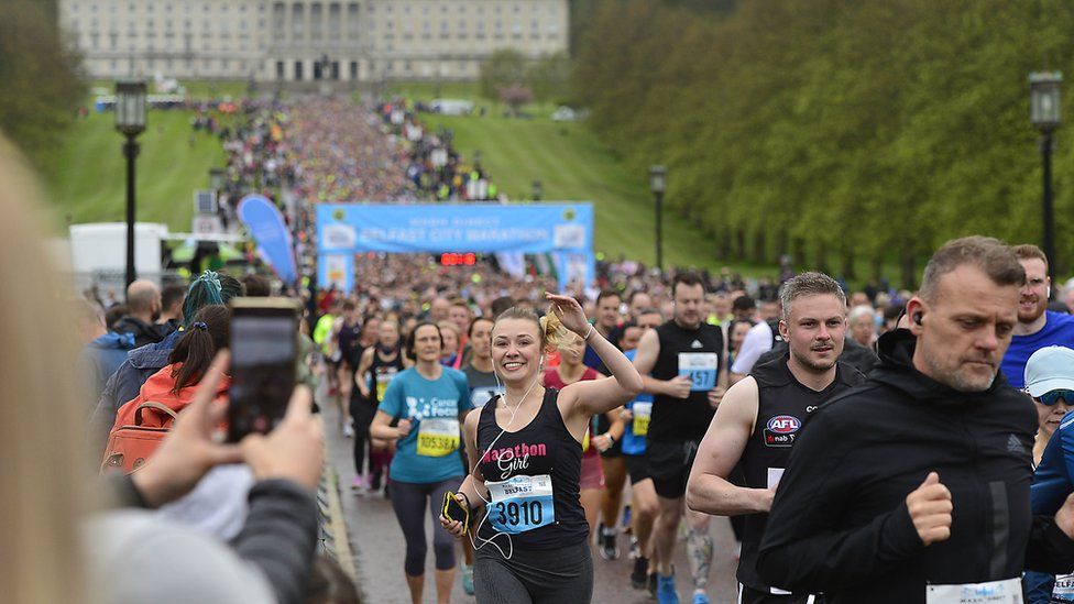 The start of the 2023 marathon. One girl is smiling and waving as thousands start to run