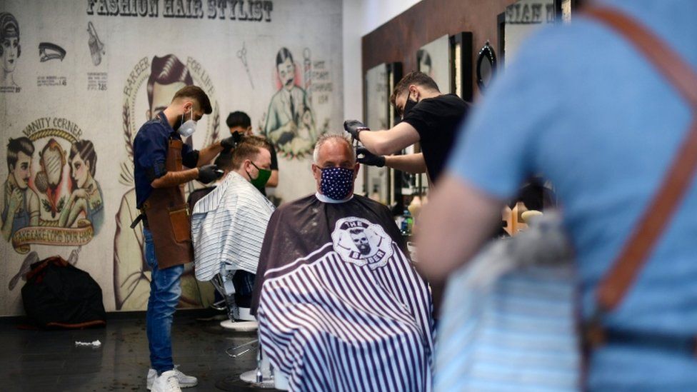 Hairdressers wearing masks cut customers' hair in a salon in Dortmund, Germany
