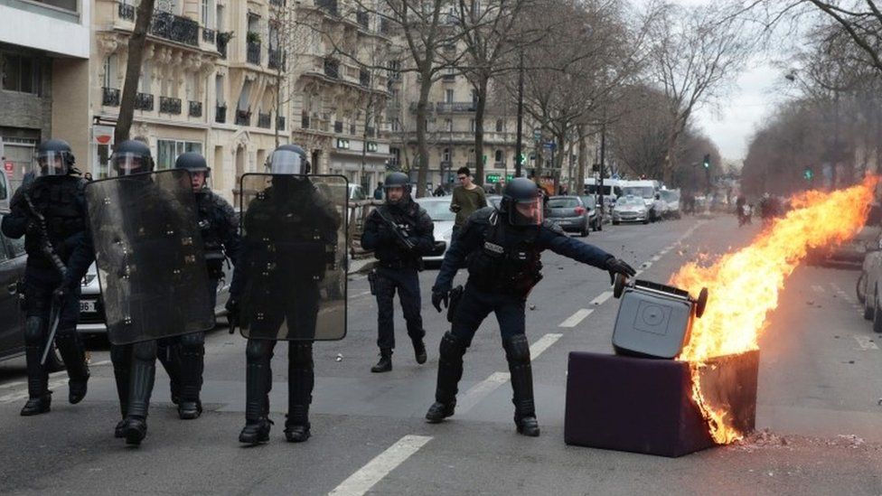 A member of the riot police removes a garbage bin from a fire started by demonstrators protesting against alleged police brutality in Paris (23 February 2017)