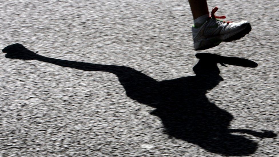 A runner casting their shadow on the road