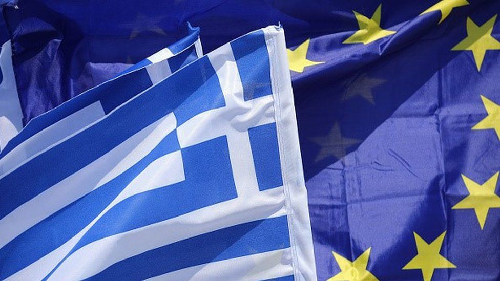 An EU flag and flags of Greece flutter in the wind