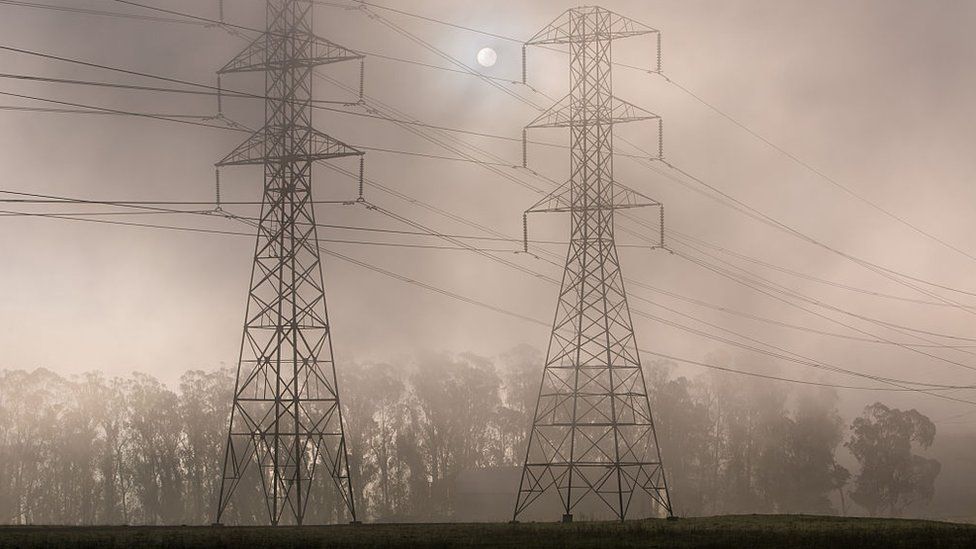 Power pylons shrouded in smoke with the sun behing