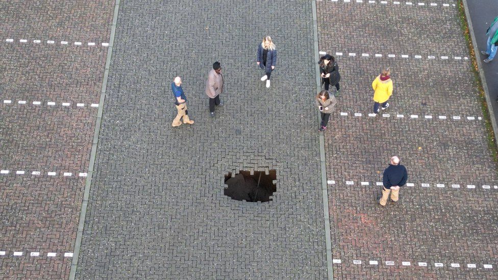 sinkhole in car park with people standing around it