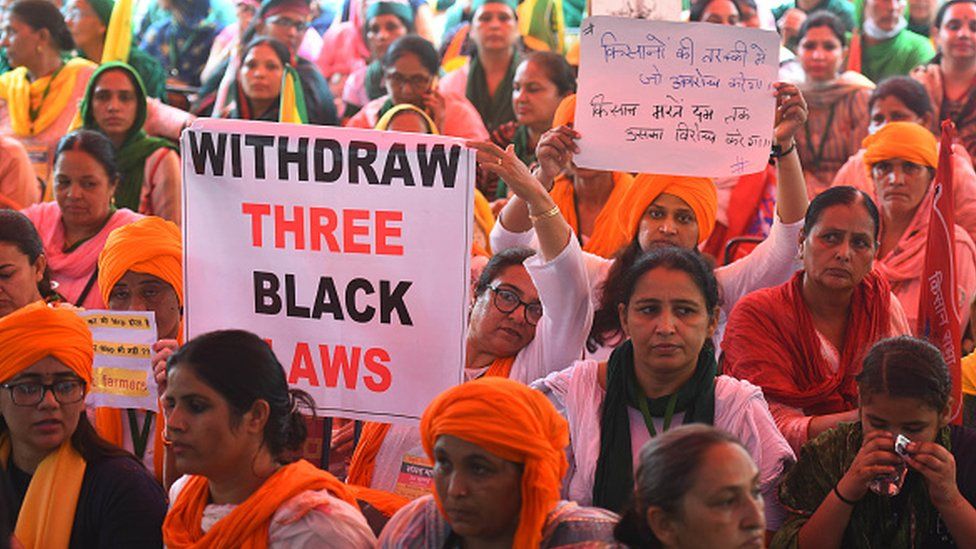 A woman sitting with a poster as part of a group during a protest against the new farm laws at Jantar Mantar on July 26, 2021