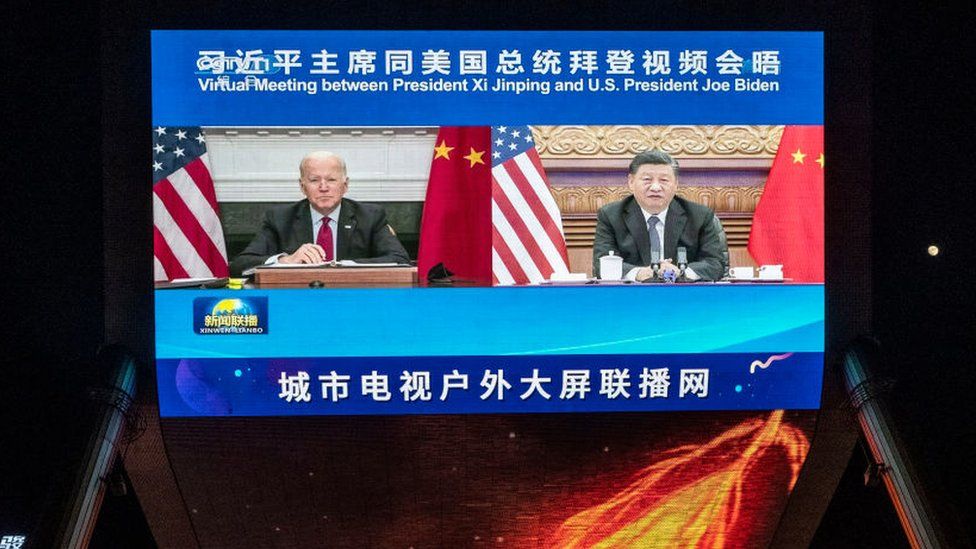 На большом экране показаны президент США Джо Байден (слева) и президент Китая Си Цзиньпин во время виртуального саммита, когда люди проходят мимо во время вечерних новостей CCTV, транслируемых возле торгового центра 16 ноября 2021 года в Пекине, Китай.