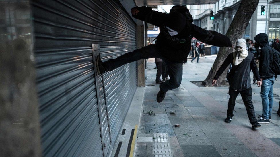 A protester kicks to break the shutter of a business along the street