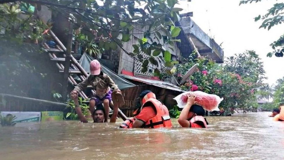 A man carries a boy on his shoulder as they walk through a flooded road in Capiz Province with the aid of rescuers