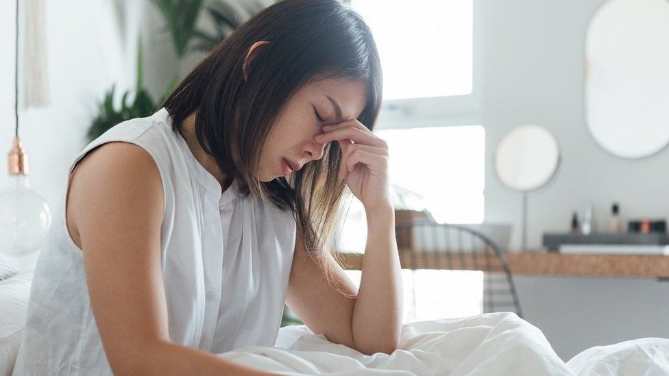 Молодая женщина трогает переносицу, чтобы облегчить головную боль во время отдыха в постели.