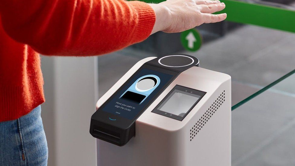 A person's arm and torso in frame show them holding a hand over a scanning terminal which has a ring pointing upwards, and the instruction to "move your palm to align the circles"