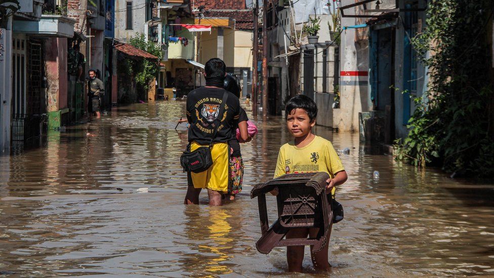 A boy carrying a chair walks through a submerged road in Indonesia