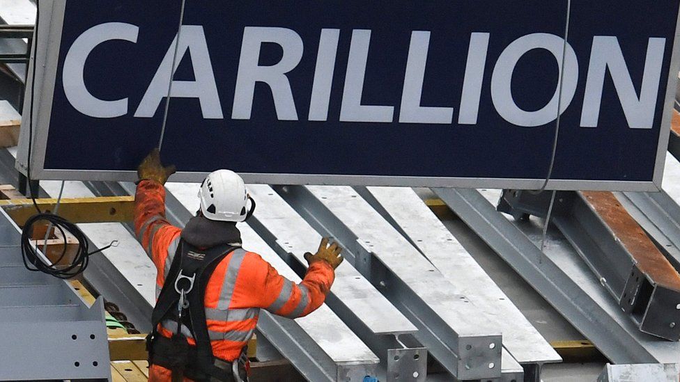 A construction worker guides down a sign showing the name of Carillion