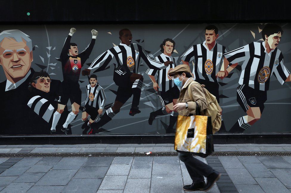 man walks past Newcastle United mural