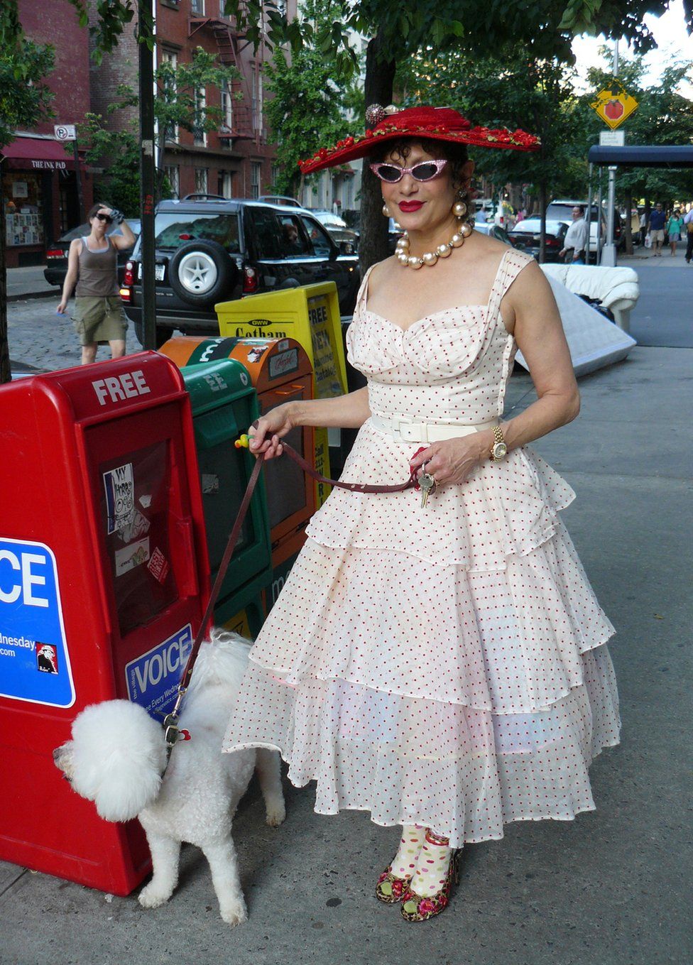 A woman dressed in an 1950s-style polka dot dress walks her dog