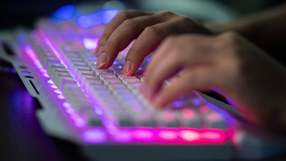 A photograph of a lit up keyboard and somebody's hands typing