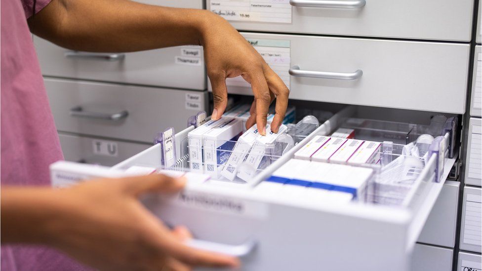 Close-up of a female pharmacist searching for prescription medicine in storage rack. Woman hands looking for medicine in a storage rack in the hospital pharmacy store.
