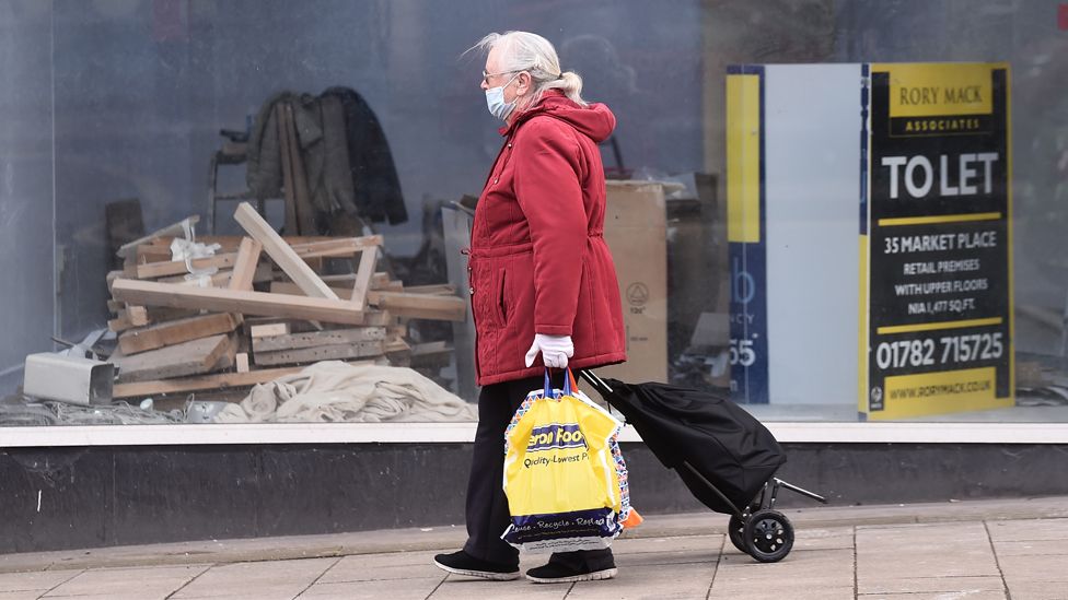 A woman wearing a mask walks past an empty shop which is to let on 15 March 2021 in Burslem, England