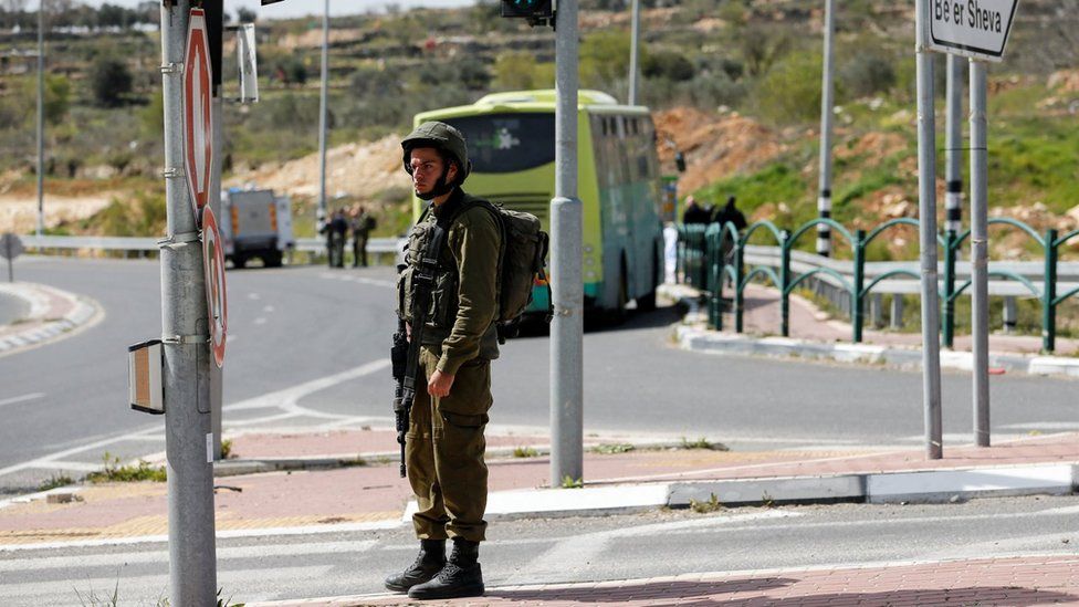 Израильский солдат стоит на месте ножевого нападения в блоке поселений Гуш-Эцион на оккупированном Западном берегу (31 марта 2022 г.)