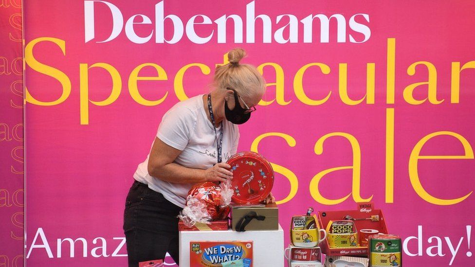 A shop assistant adjusts a window display in Debenhams in front of a sale sign