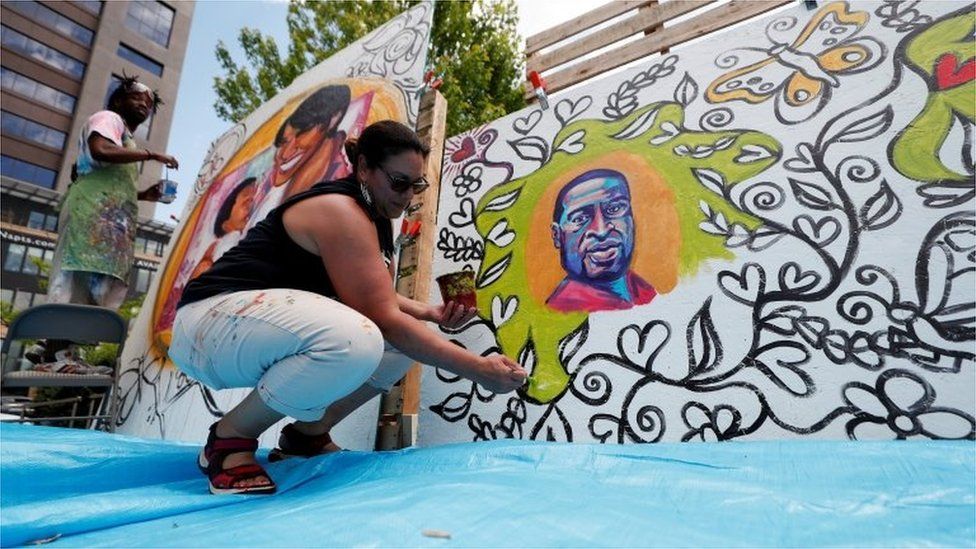 A woman paints a memorial to George Floyd on the anniversary of his murder