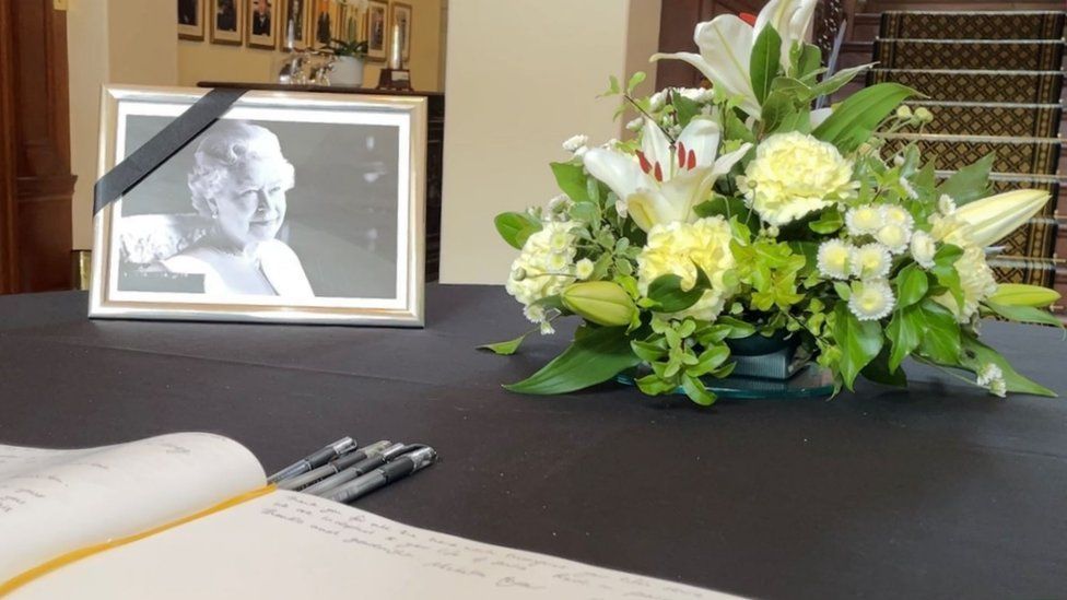 Picture of the Queen on a table next to a book of condolence and some flowers