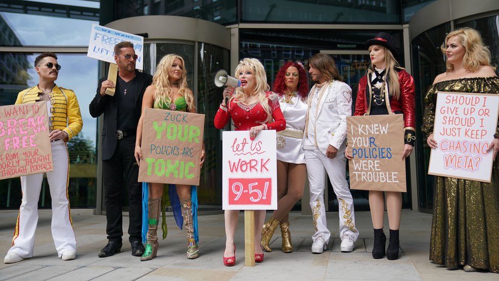 A line of eight tribute artists outside the Meta office, with Dolly Parton centre holding a megaphone