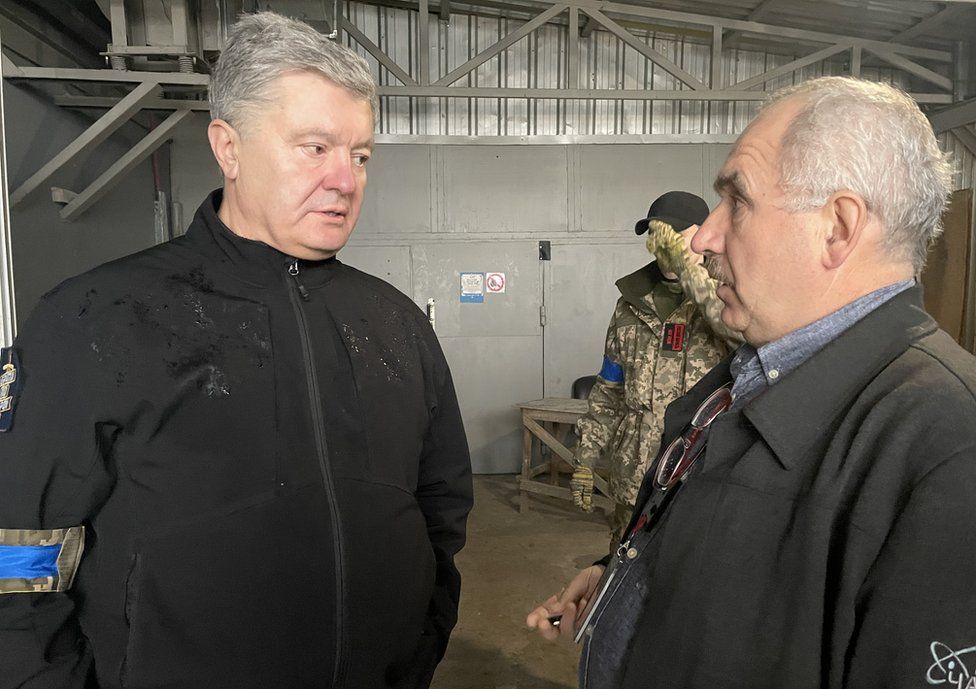 Petro Poroshenko, Ukraine's former president, in a weatherproof jacket, speaks seriously to a man inside the Chernobyl plant