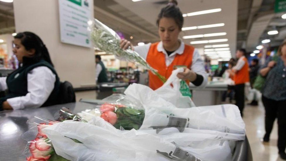 A sales assistant puts customers goods on plastic bags at a supermarket in Santiago, on July 18, 2018.