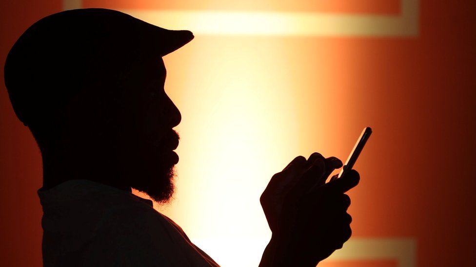 A silhouetted man types on his phone in low light conditions