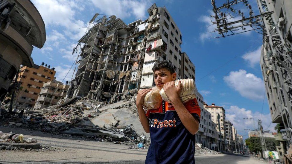 A Palestinian youth carrying bread walks past buildings destroyed in recent Israeli strikes in Al Remal, in Gaza City, 16 October 2023