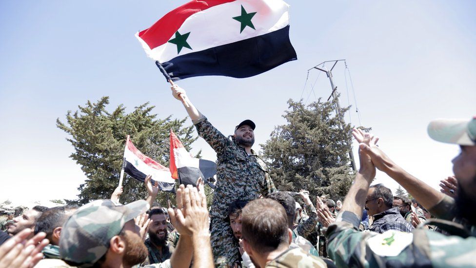 Syrian soldiers wave the Syrian national flag in the city of Quneitra, in the Golan Heights (27 July 2018)