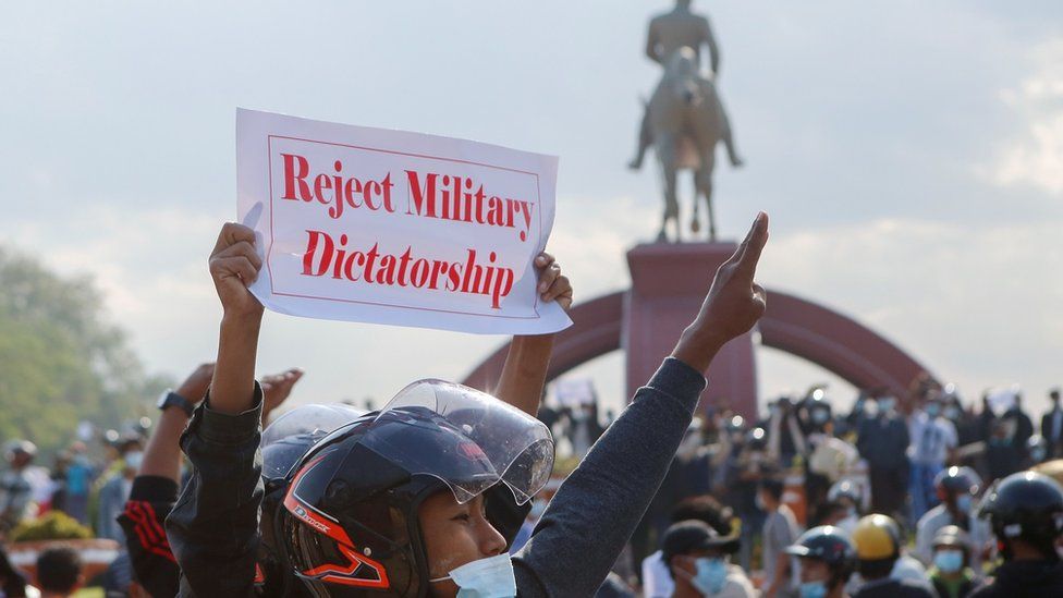 A protester holds up a placard as another gives the three-finger salute during a demonstration against the coup and to demand the release of elected leader Aung San Suu Kyi, in Naypyitaw,