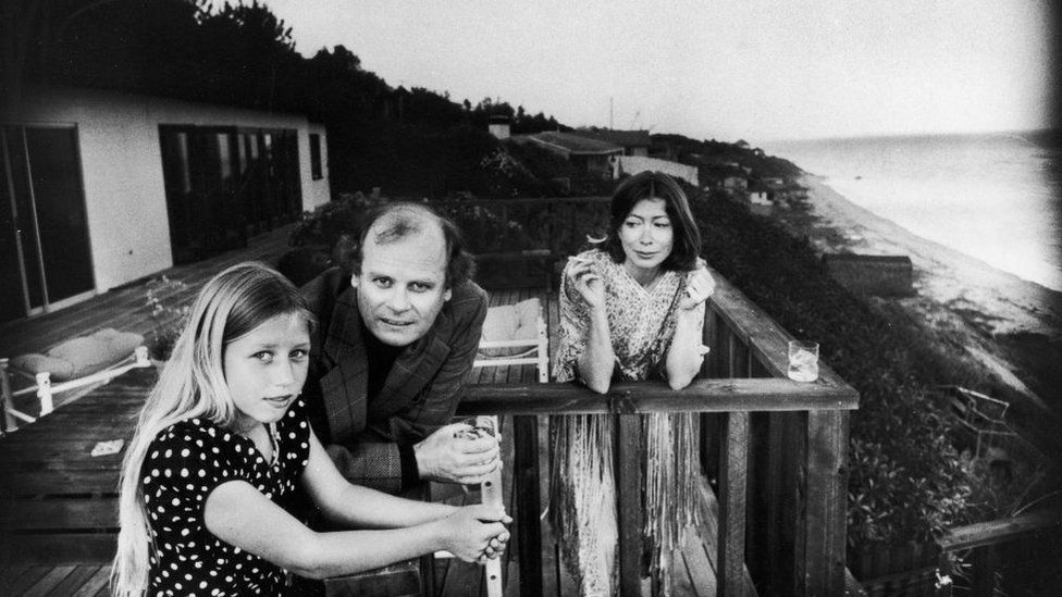 On a patio deck overlooking the ocean, Quintana Roo Dunne (L) leans on a railing with her parents, American authors and scriptwriters John Gregory Dunne (1932 - 2003) and Joan Didion, Malibu, California, 1976