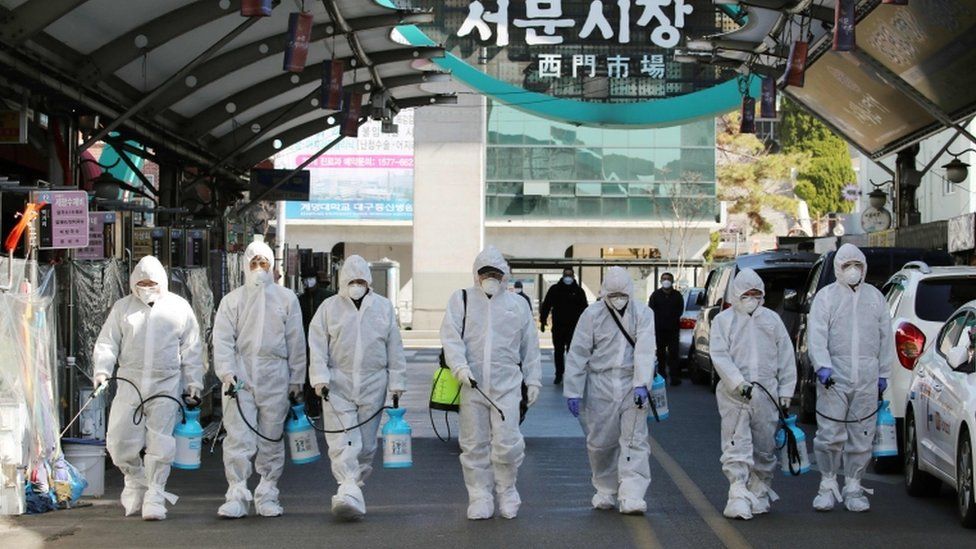 Market workers wearing protective gear spray disinfectant at a market in the south-eastern city of Daegu on February 23, 2020