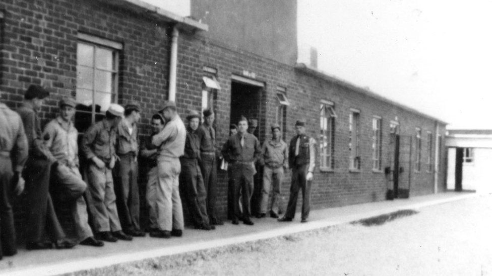 An old black and white photo of soldiers queuing outside a red brick building.