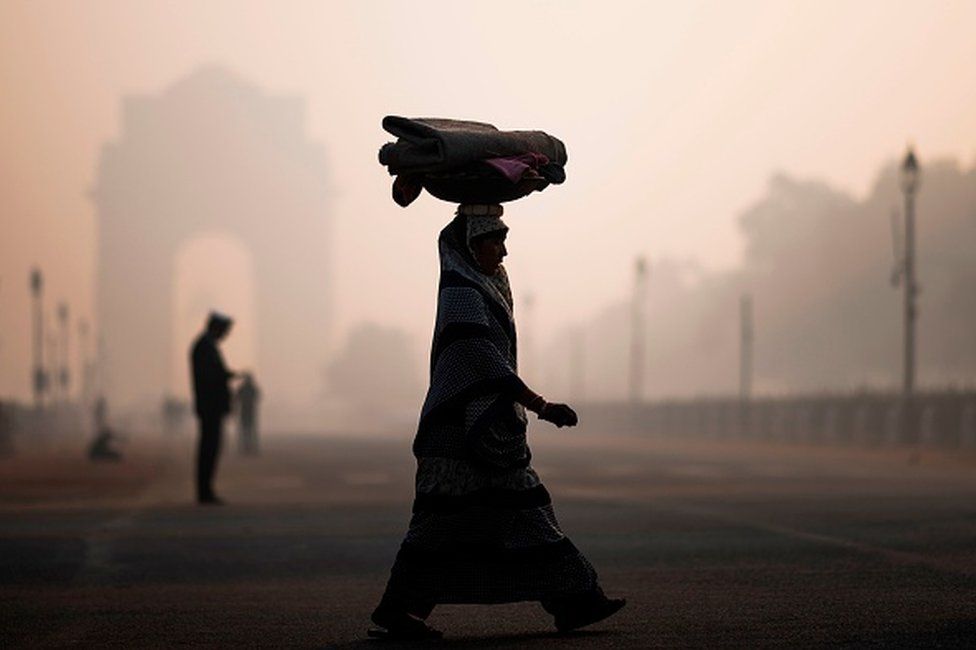 A woman balances a load on her head as she crosses a street near India Gate in heavy smoggy conditions in New Delhi on December 6, 2019