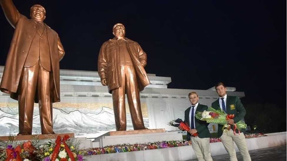 Two Australians pose for a photo in front of a monument in North Korea