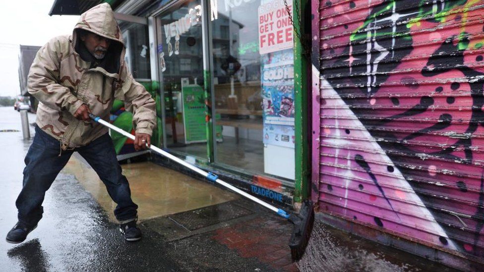 A man sweeps water in front of a shop