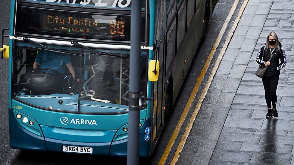 A pedestrian walks past a bus in Liverpool, north west England on October 12, 2020