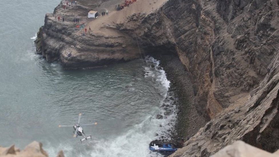 A helicopter helps rescue workers at the scene after a bus crashed with a truck and careened off a cliff along a sharply curving highway north of Lima, Peru, January 2, 2018