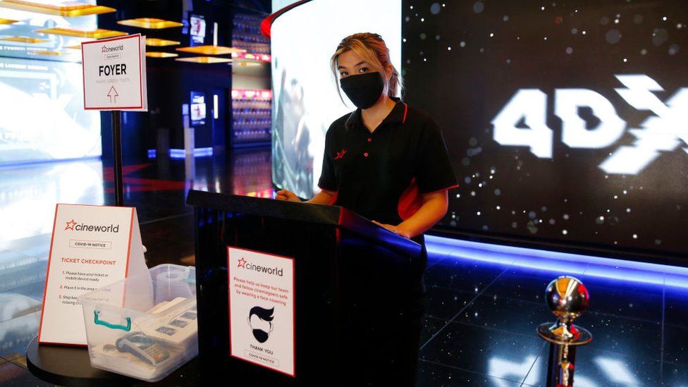 Woman standing behind counter in Cineworld cinema wearing facemask