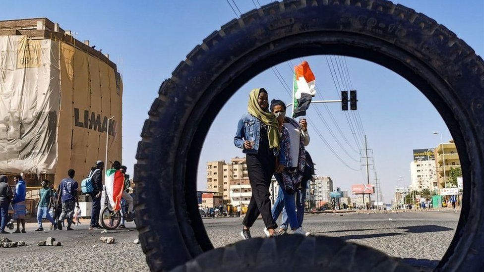 A woman carries a national flag as protesters block a street in the Sudanese capital Khartoum, during a demonstration against the killings of dozens in a crackdown since last year's military coup, as US diplomats pressed for an end to the violence, on January 20, 2022.