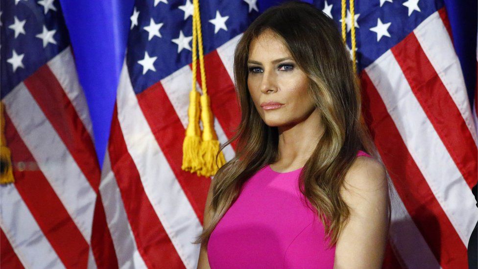 Melania Trump standing in front of an American flag